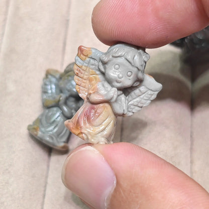 Close up view of a mini carved angel figurine with tan and reddish highlights displayed in hand
