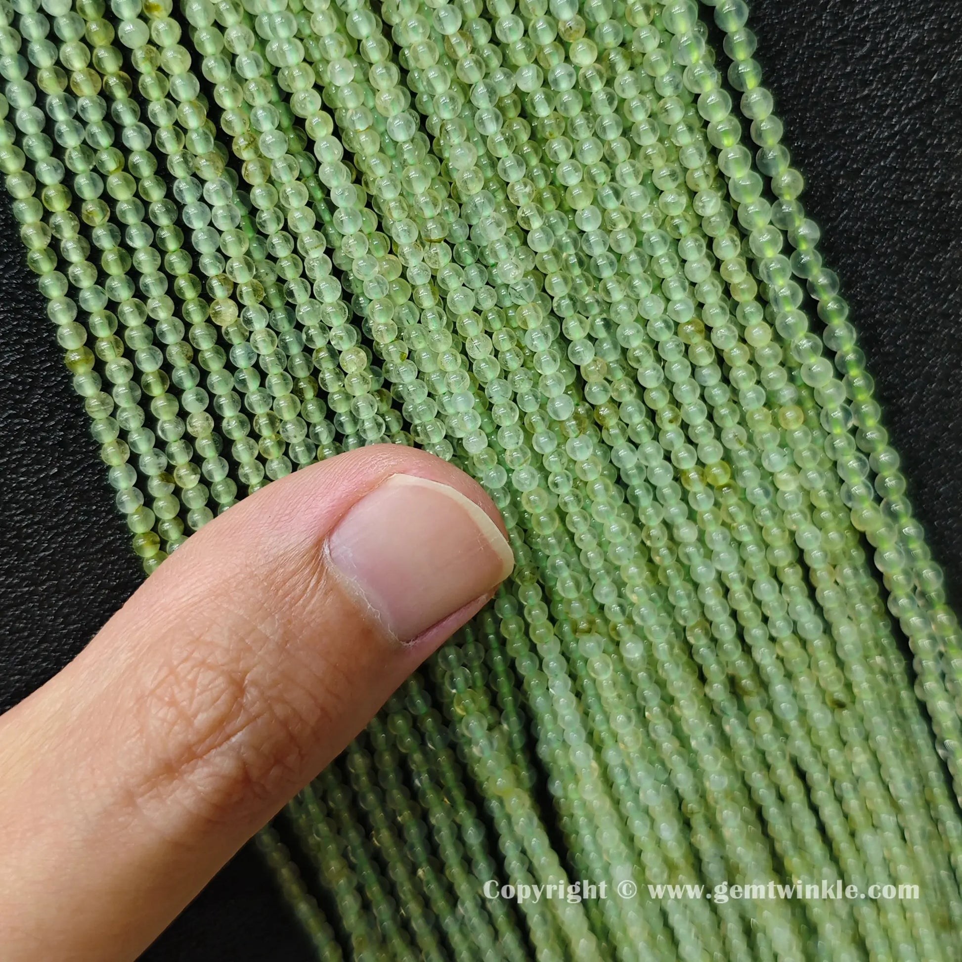 Perspective view of clean 3mm pale green prehnite round beads showing smooth polish