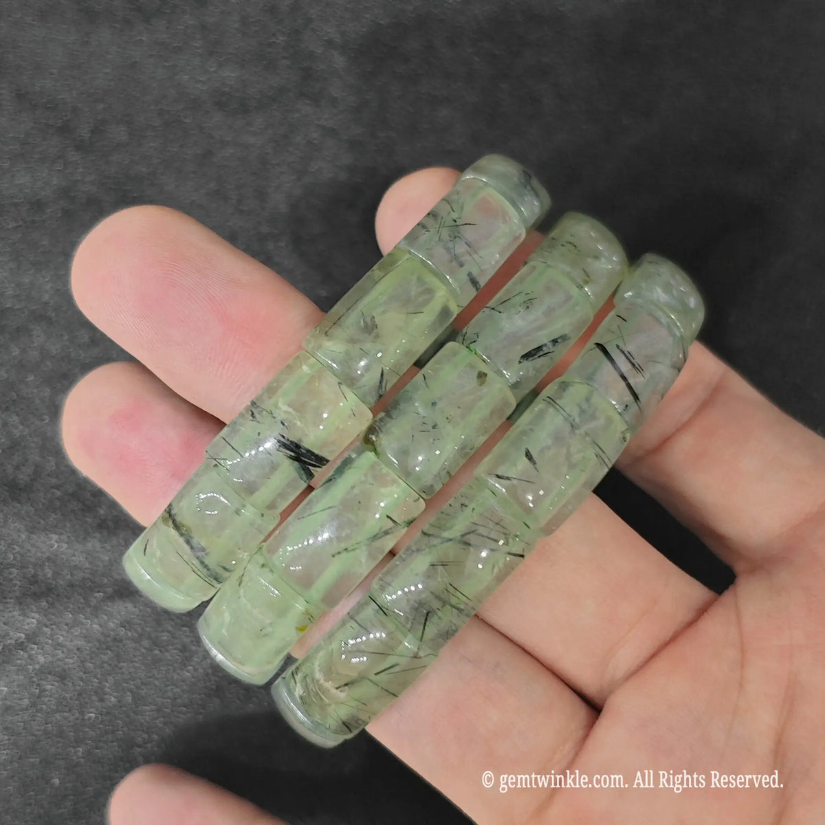 Three prehnite with black tourmaline plate bead stretch bracelets held across hand demonstrating ready-to-sell boutique stock