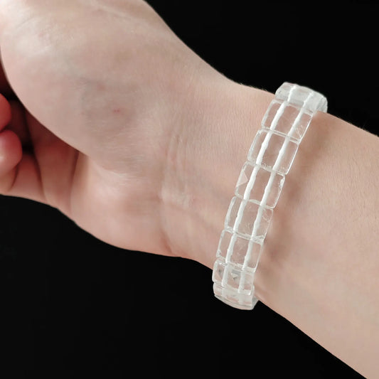 Natural clear quartz faceted beads (~12mm length), multi-cut surfaces, high clarity, stretch elastic—held in hand on black background