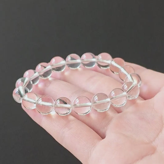 Collector-grade natural clear quartz bracelet with near-inclusion-free 10mm round beads; held in hand on black background, showcasing exceptional transparency and glassy luster for spiritual jewelry lovers