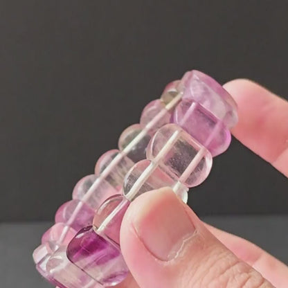 Natural multicolor fluorite oval bead bracelet held in hand, showing purple-to-pink-to-clear gradient and faceted surface on black background