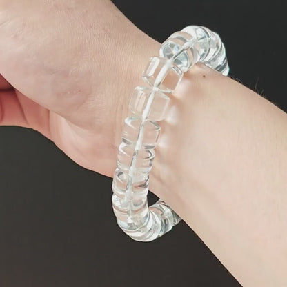 Natural clear quartz rondelle beads (~13mm diameter), smooth polished edges, high clarity, stretch elastic—held in hand on black background
