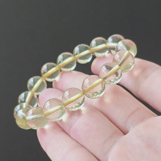 Natural clear lemon citrine round beads (~10mm), high clarity, no inclusions, stretch elastic—held in hand on black background