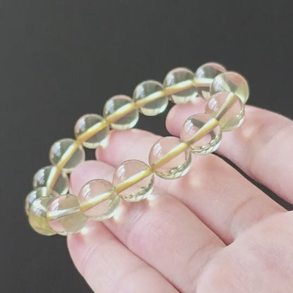 Natural clear lemon citrine round beads (~10mm), high clarity, no inclusions, stretch elastic—held in hand on black background