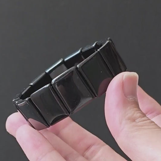 Black obsidian square bead handchain held in hand, glossy finish, minimalist design on dark background