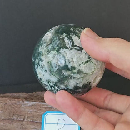 Natural moss agate sphere (approx. 6.5cm), D variant with vivid green dendritic inclusions on milky white chalcedony; displayed on natural wood base for altar or desk decor