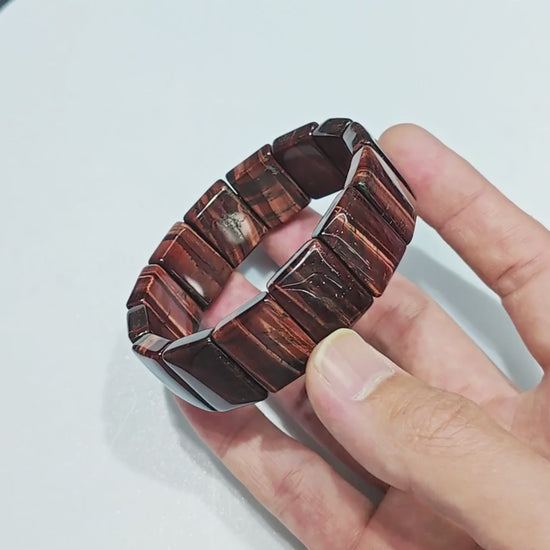 Hand holding natural red tiger eye elastic bracelet with 20mm rectangular beads and deep red-brown bands