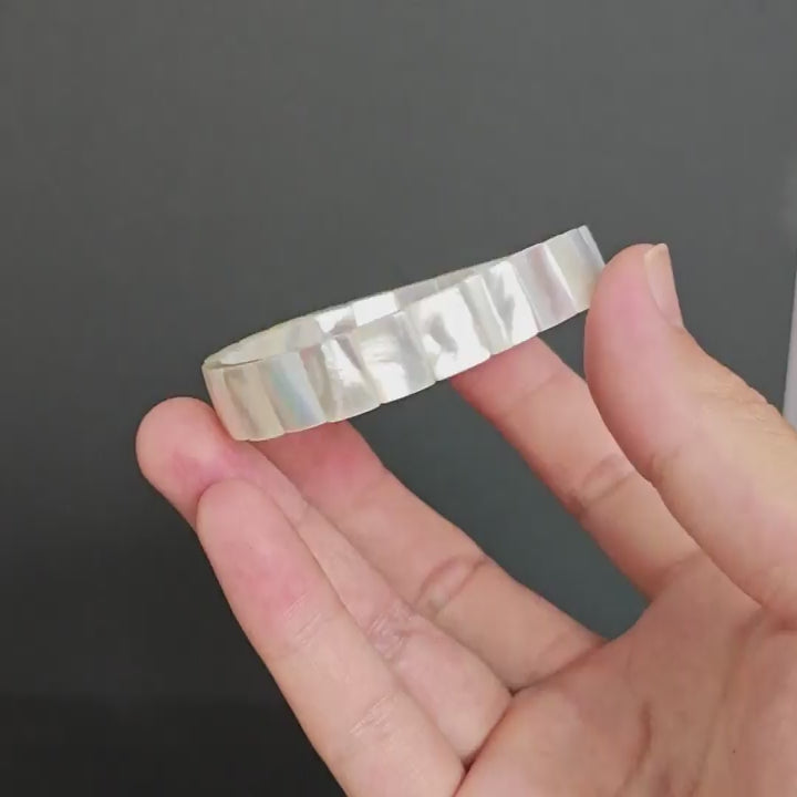 Natural white mother-of-pearl rectangular bead bracelet held in hand, showing creamy base with silver-pink iridescence on dark background