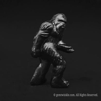 Full profile view of a protective black obsidian bigfoot figurine showcasing glossy volcanic dark surface and hand carved details