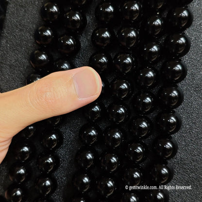 Hand holding highly reflective natural pure black obsidian crystal beads strands from 6mm to 20mm