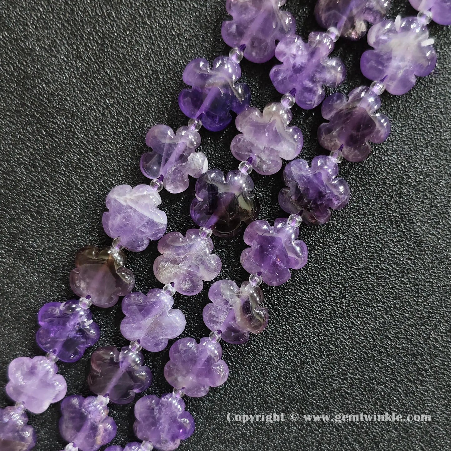 Angled view of natural purple amethyst floral carved gemstone strands laid together