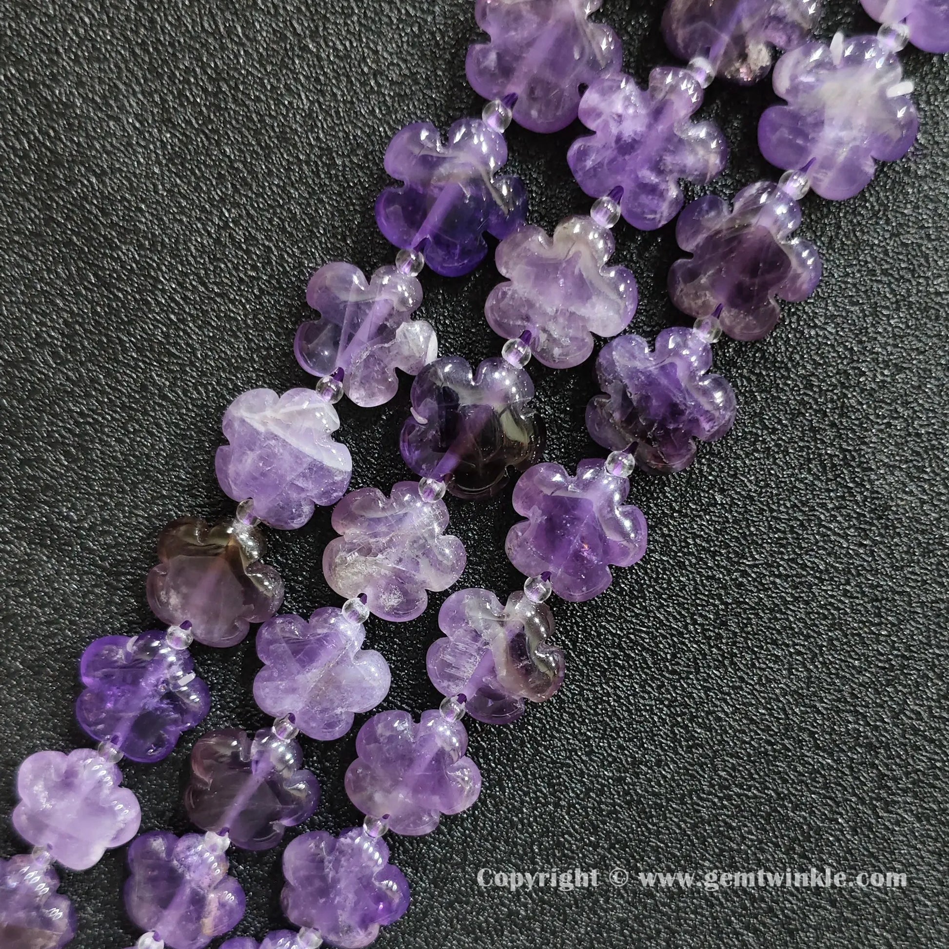Angled view of natural purple amethyst floral carved gemstone strands laid together