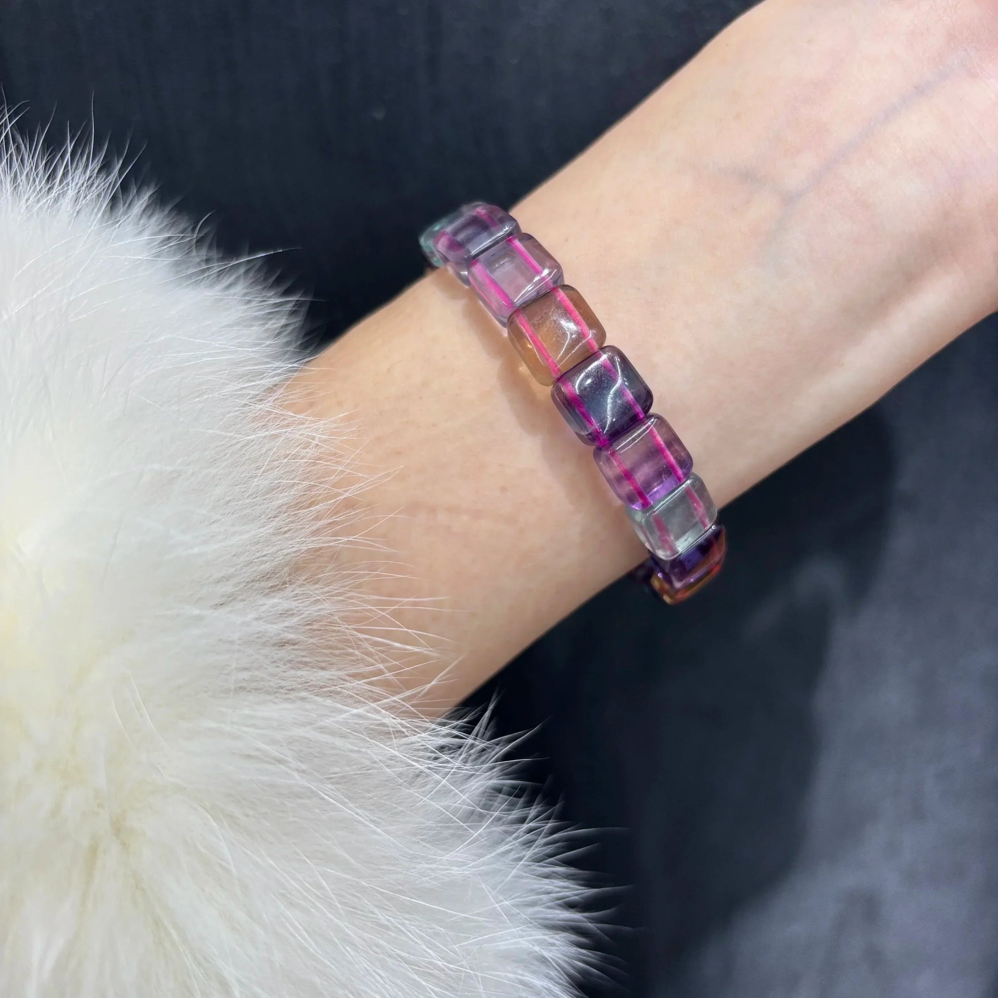 Close-up of a hand wearing the Natural Rainbow Fluorite Square Bead Bracelet, showing how it fits on the wrist with a white fur sleeve.