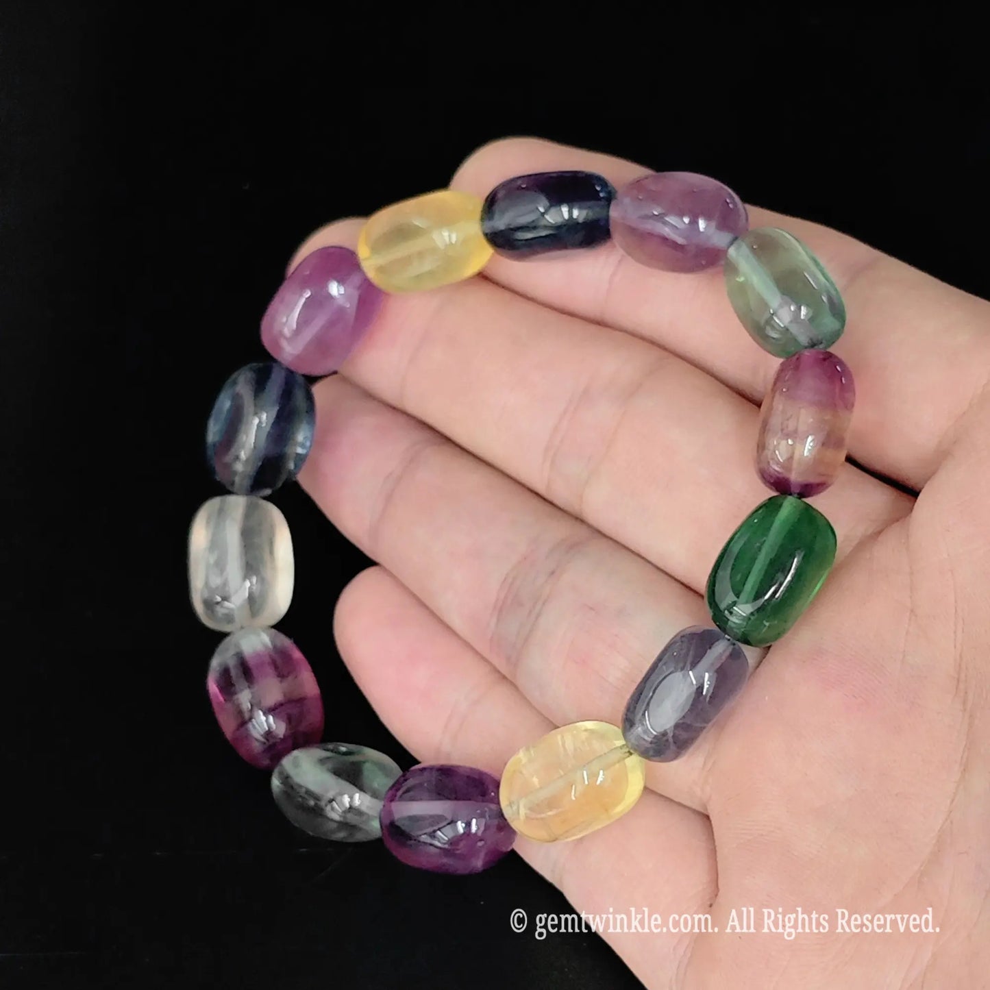 multi-color rainbow fluorite drum bead stretch bracelet displayed in open hand