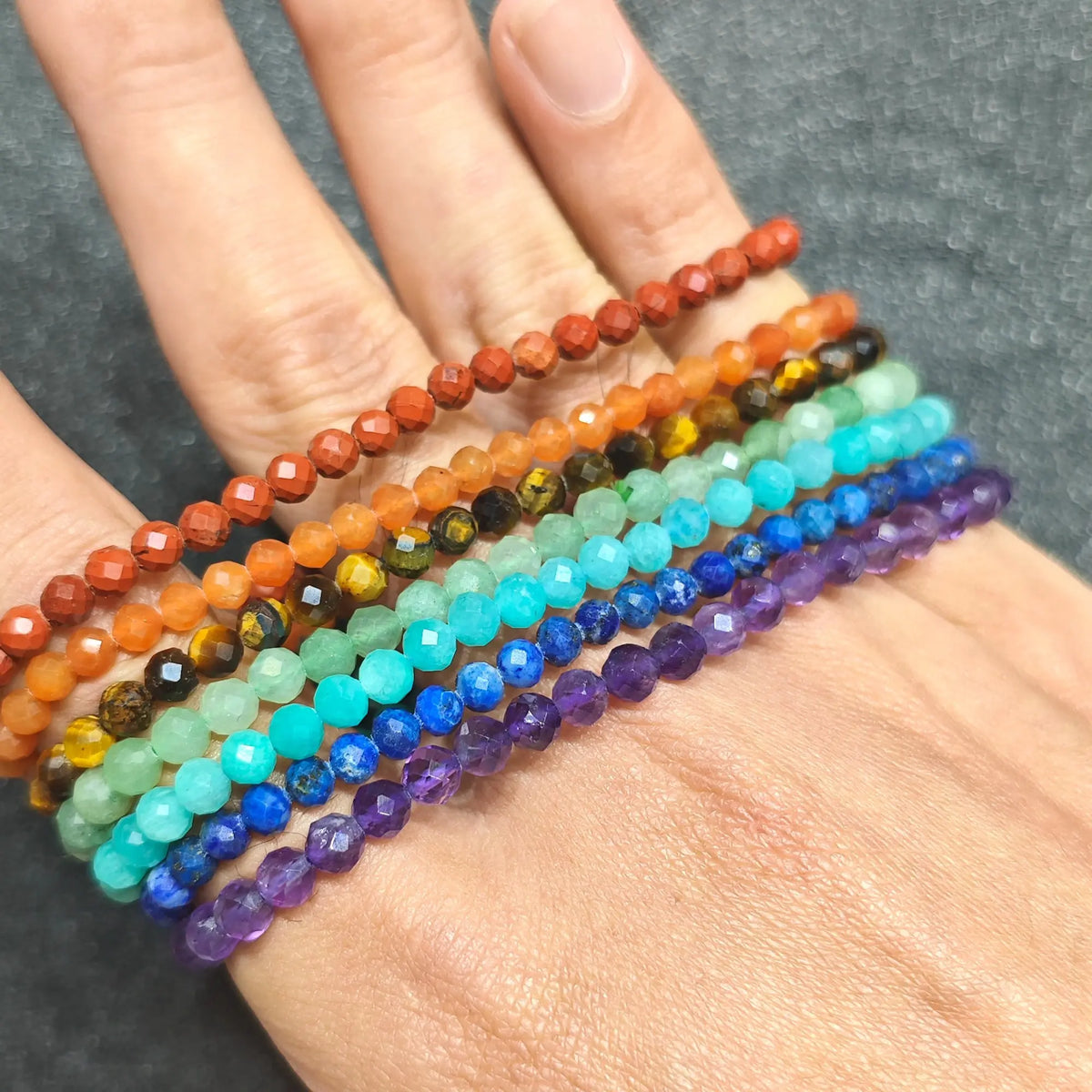 7 piece rainbow gemstone faceted bead stacking stretch bracelets lined up neatly across back of hand