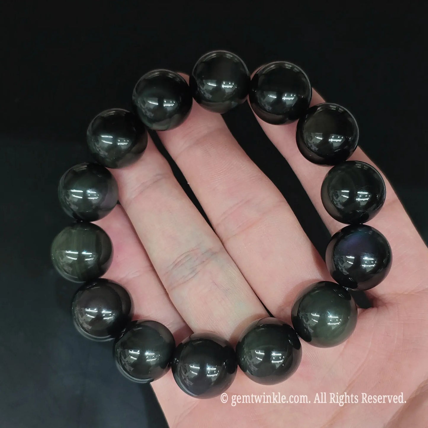 Full view of rainbow eye volcanic obsidian round bead stretch bracelet resting open on hand showcasing smooth beads