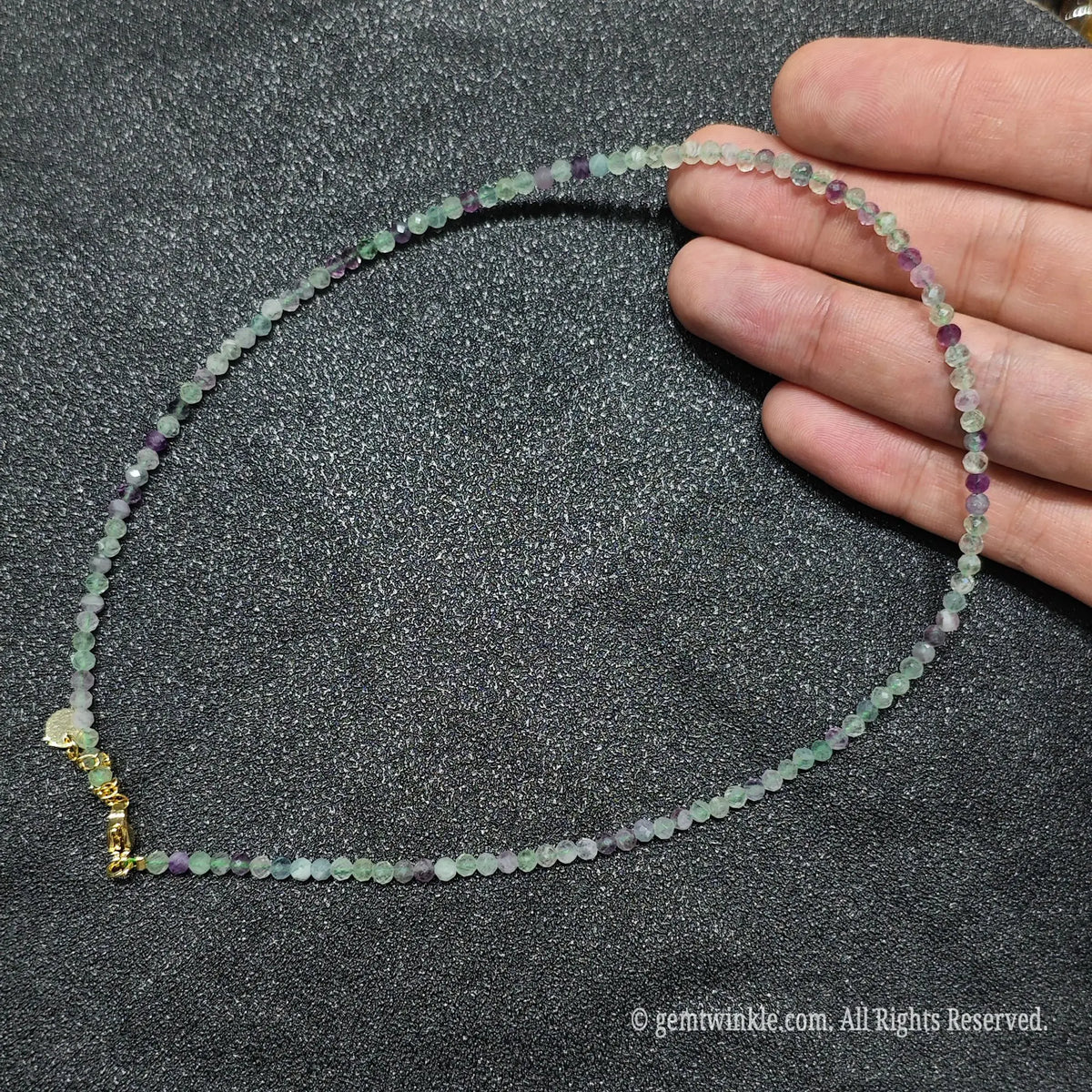 Hand holding 3mm faceted rainbow fluorite necklace showing purple and green crystal clarity and gold lobster clasp