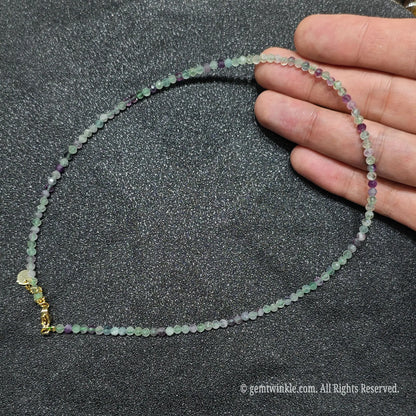 Hand holding 3mm faceted rainbow fluorite necklace showing purple and green crystal clarity and gold lobster clasp