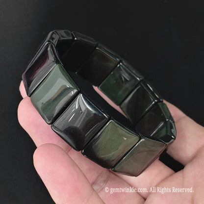 Rainbow obsidian plate cuff bracelet held in hand under lighting highlighting rainbow eye reflections