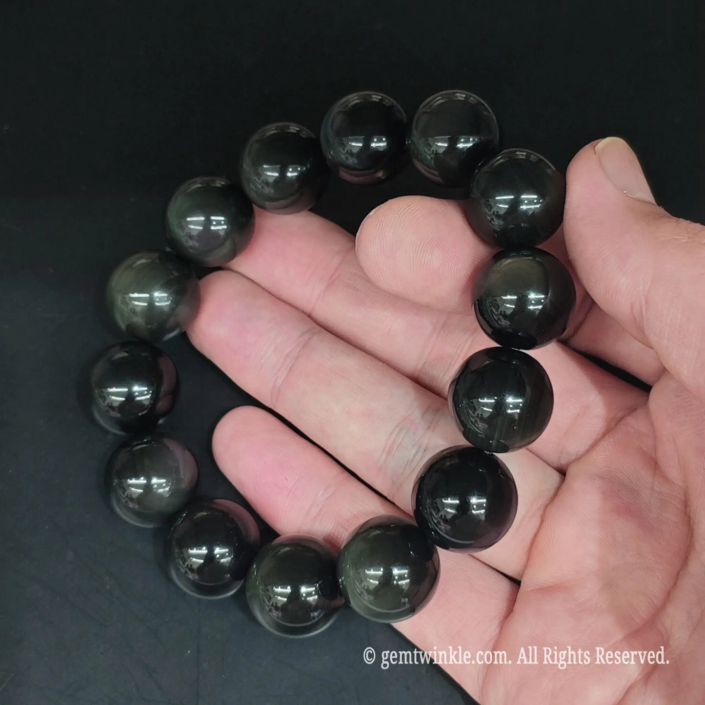 Rainbow obsidian round bead stretch bracelet styled on wrist displaying sleek fit and dark reflective sheen