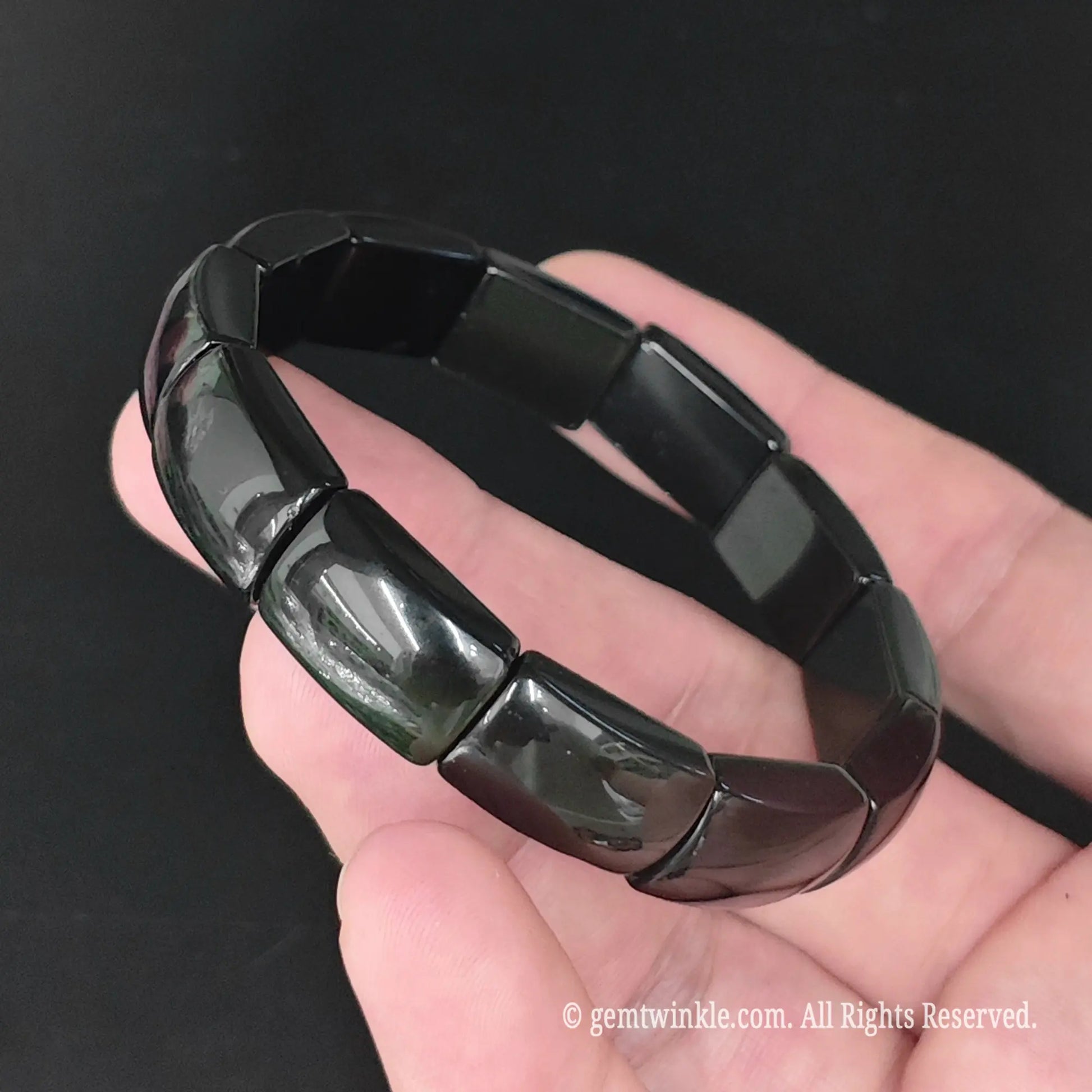 Rainbow sheen obsidian 16mm plate stretch bracelet worn on wrist displaying smooth black volcanic glass profile