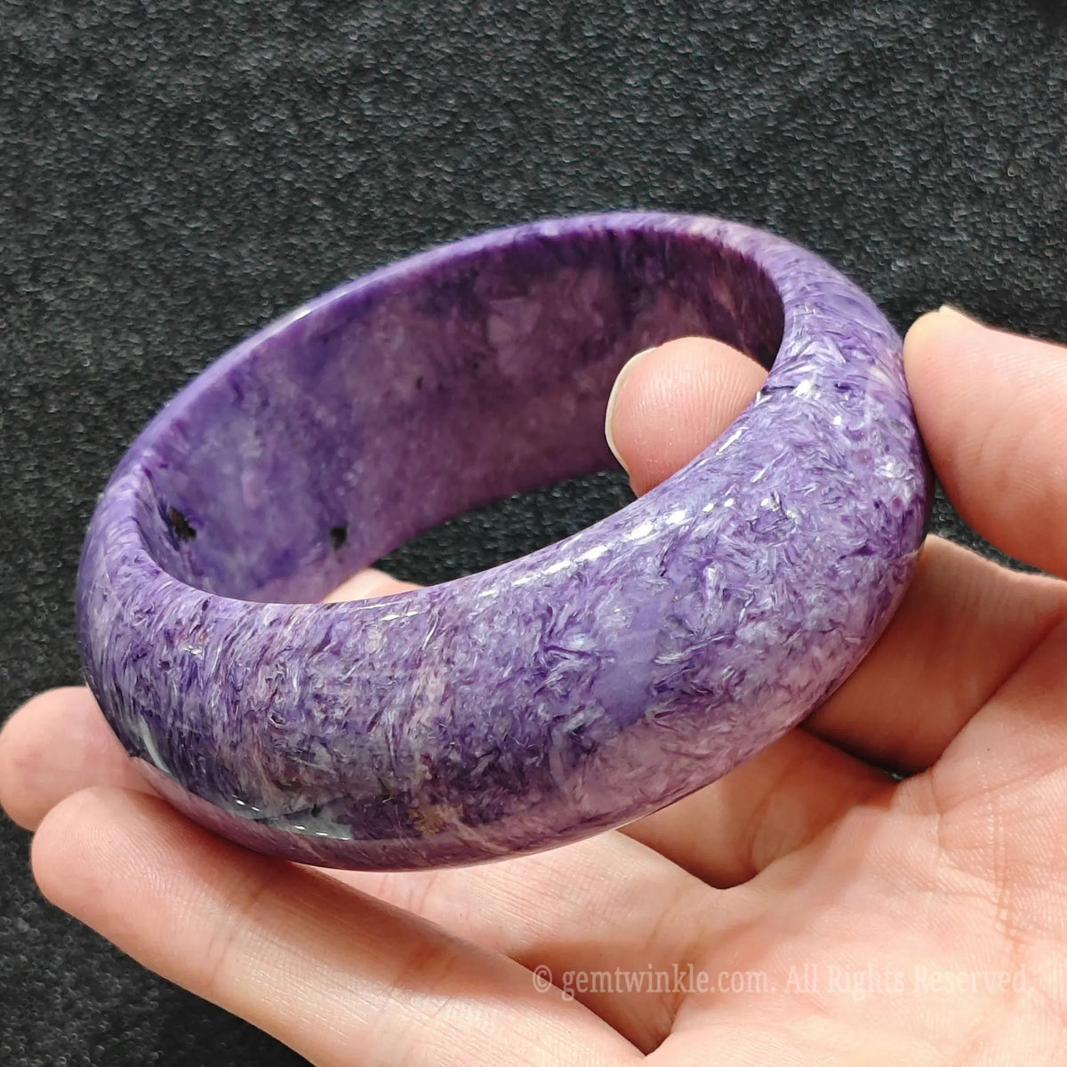 full perspective of wide purple stone bangle held between fingers