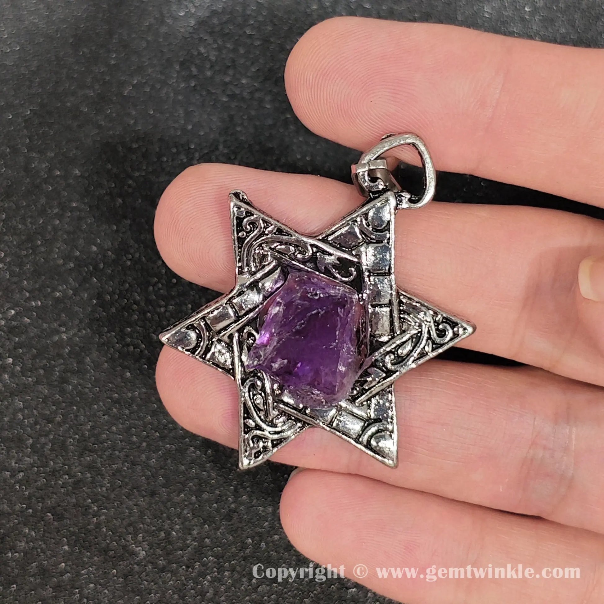 Back view of metal alloy geometric star frame enclosing rough amethyst stone with internal cloud inclusions