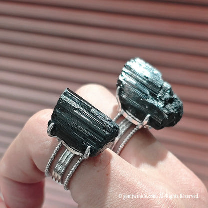 Side angle of raw black gemstone prong ring showcasing wire wrapped band structure and natural crust