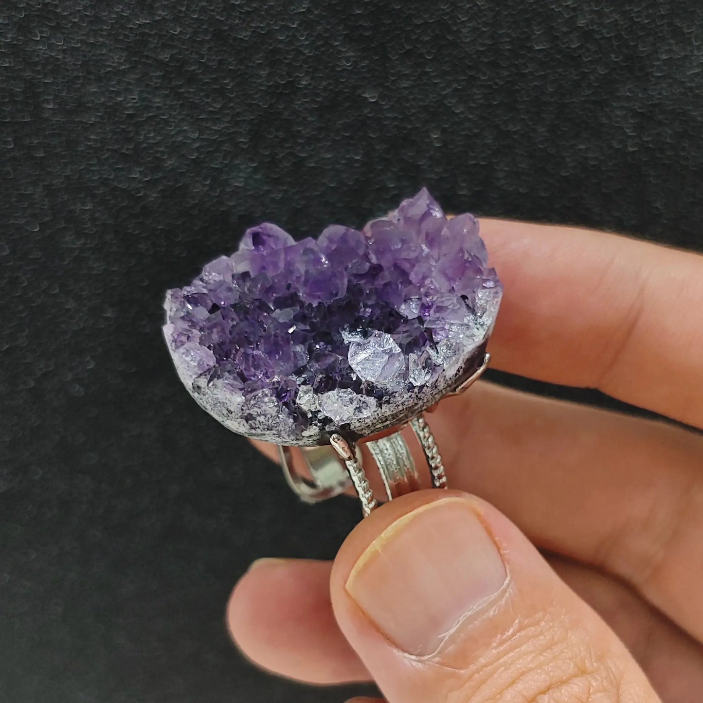 Raw amethyst crystal cluster adjustable alloy ring held in hand showcasing deep purple mineral points and textured band