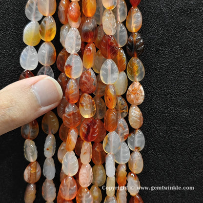 Close up view of red agate leaf carved beads held on fingers for quality preview