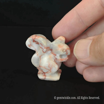 Side profile of carved red banded stone squirrel totem with creamy and brick-red patterns