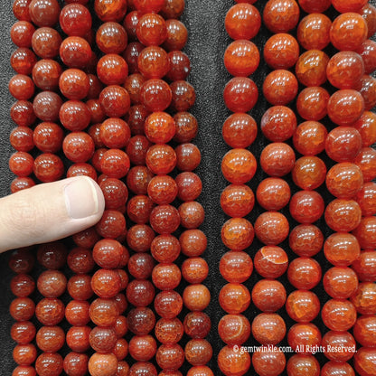Inspecting rows of red dragon veins agate beads from 6mm to 12mm held in hand with finger for boutique size verification