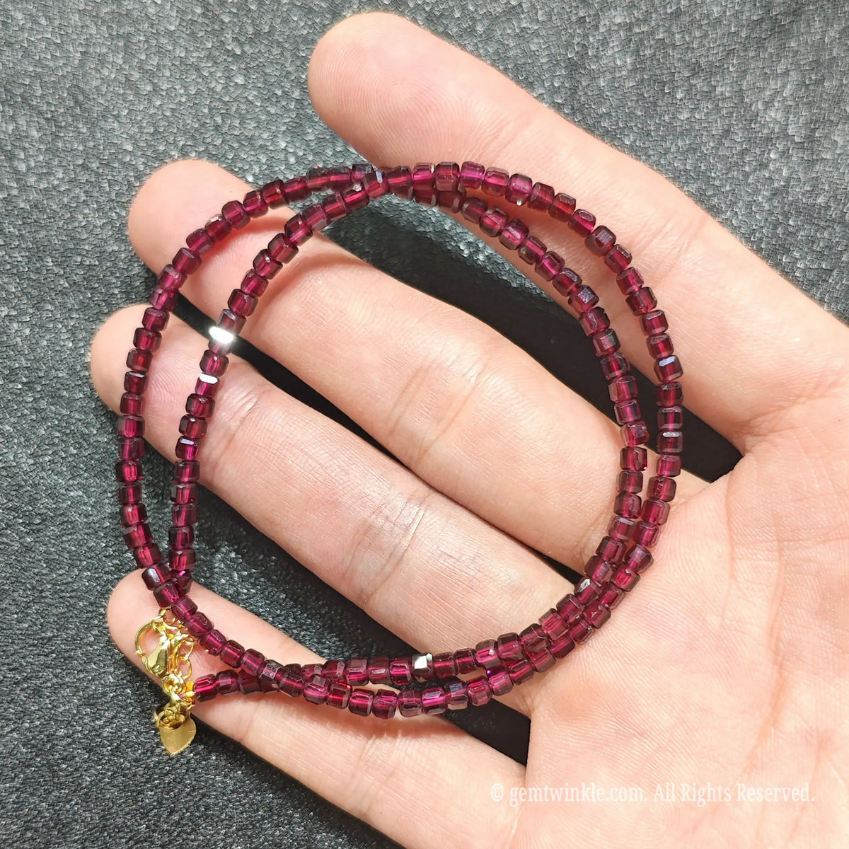 Hand holding 3mm precision cube cut Red Garnet necklace strand showing deep wine red clarity