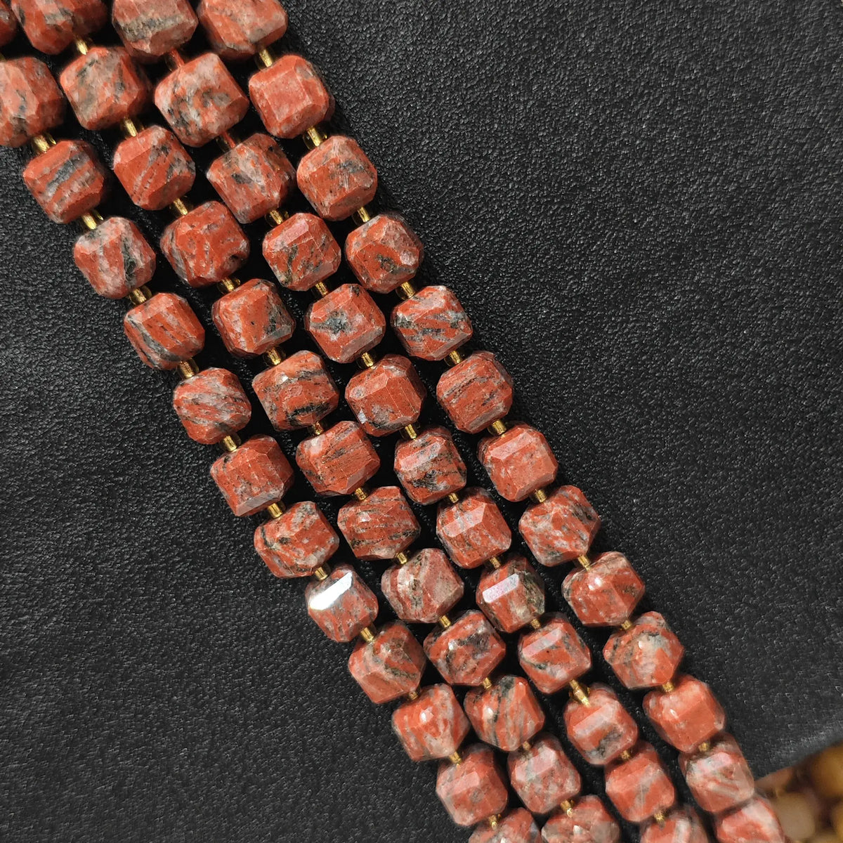 Multiple strands of red sesame jasper square beads laid out neatly for wholesale buyers