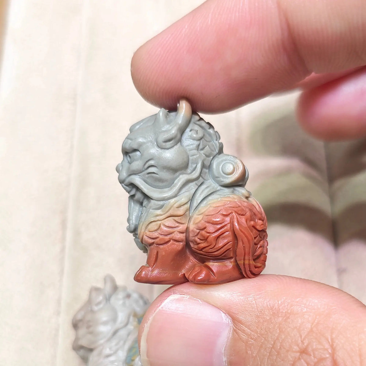 Fingertips holding a red and slate gray dual tone Kirin figurine highlighting smooth polished surfaces