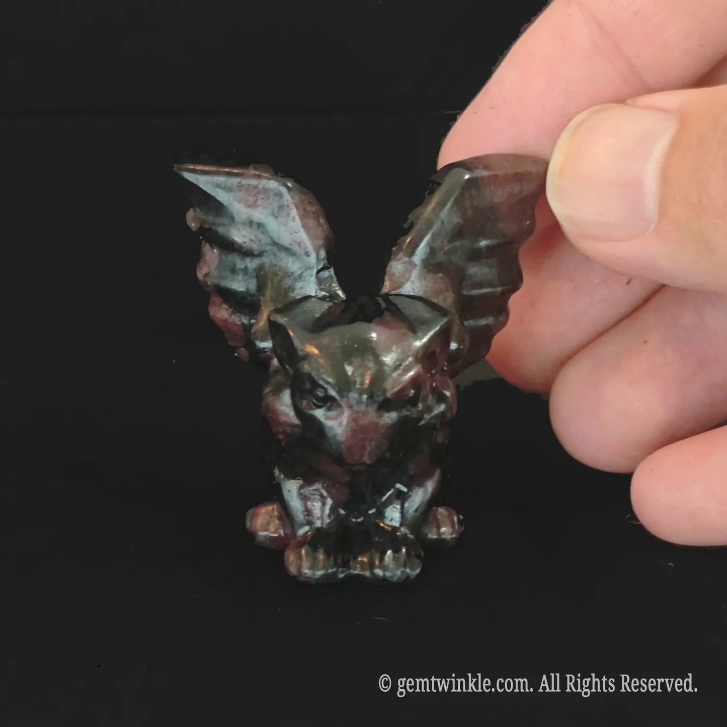 Front view of crouching red spotted stone gargoyle statue with dark crimson markings