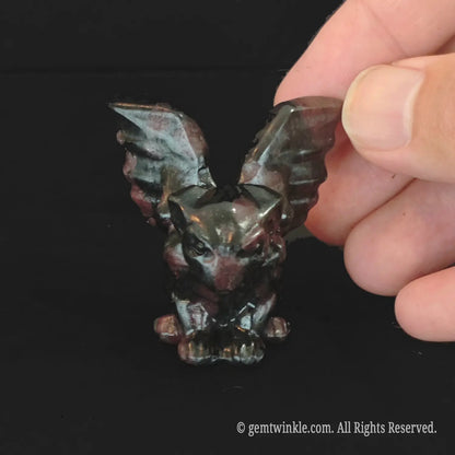 Front view of crouching red spotted stone gargoyle statue with dark crimson markings