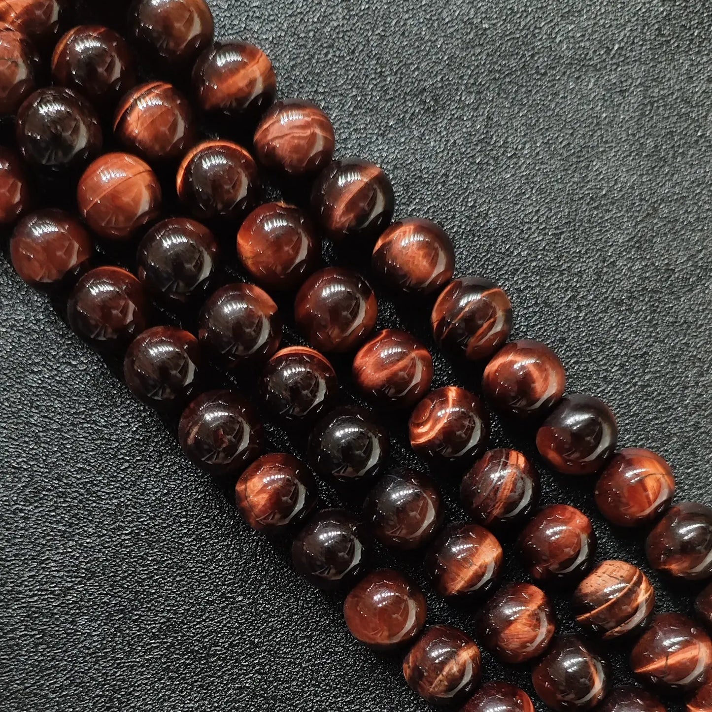 Close up of red tigers eye round beads showing smooth surface and copper chatoyancy
