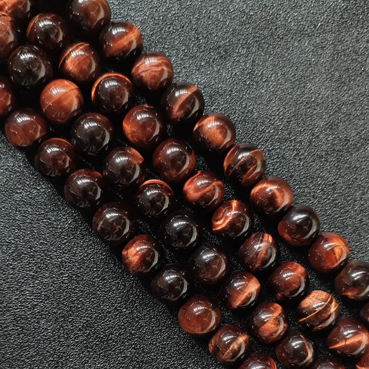 Close up of red tigers eye round beads showing smooth surface and copper chatoyancy