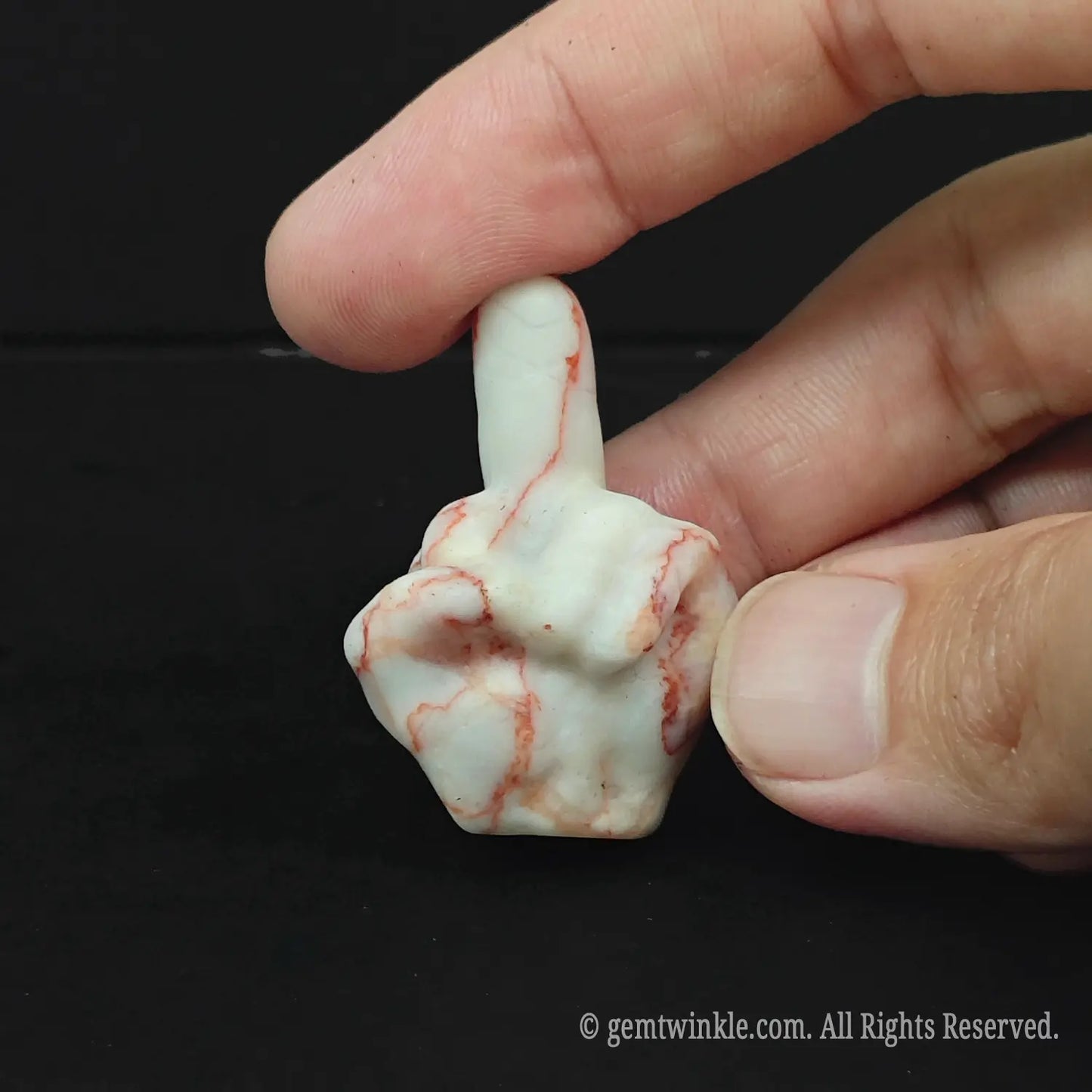 A striking red and white veined natural stone middle finger sculpture resting on a dark surface