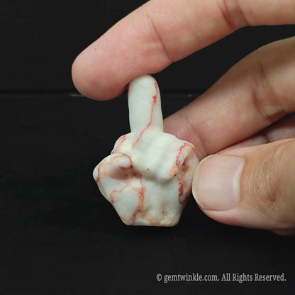 A striking red and white veined natural stone middle finger sculpture resting on a dark surface
