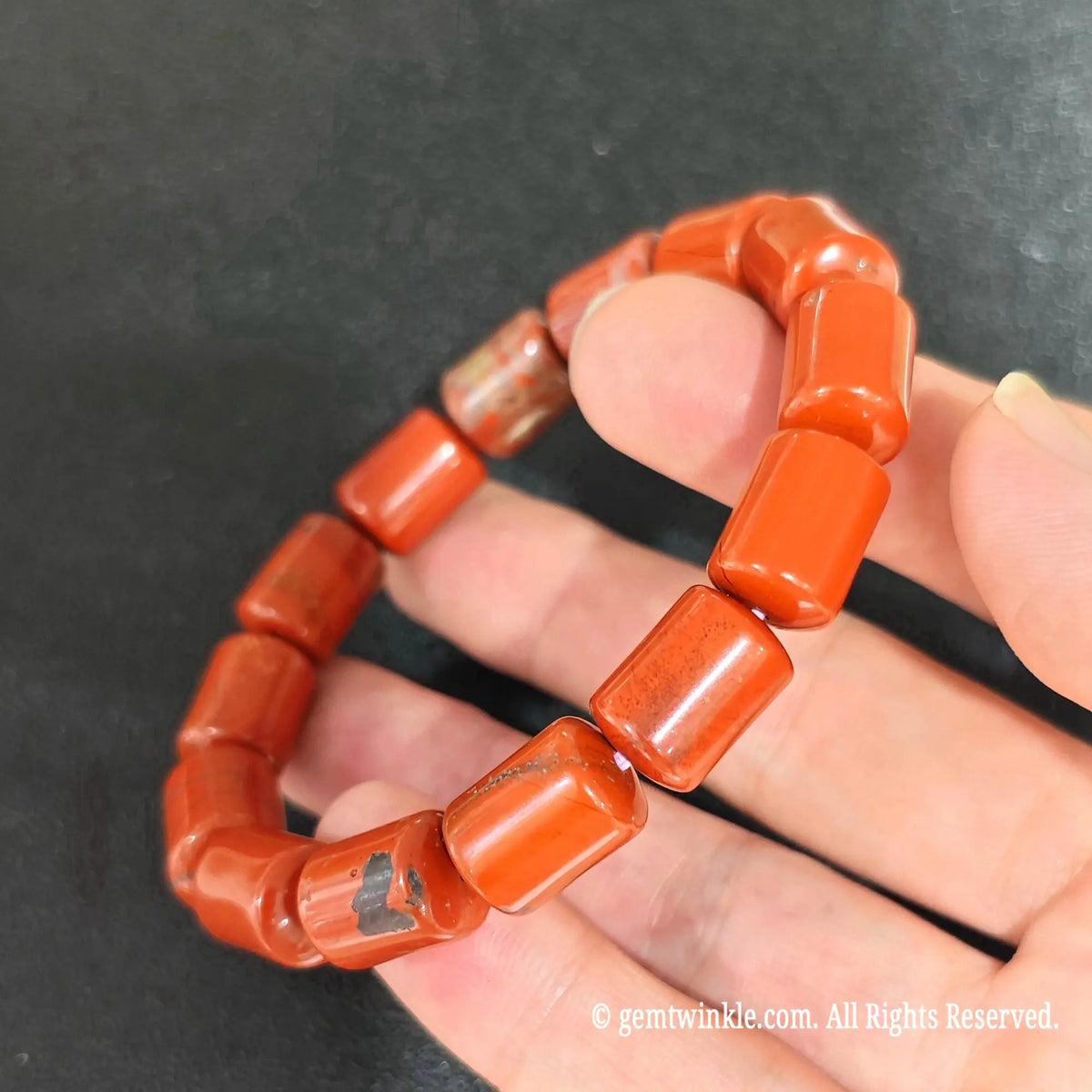 side profile of natural red jasper drum bead elastic bracelet on hand displaying smooth polished surface