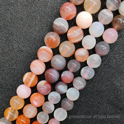 Close up view of red banded agate round loose gemstone beads showing unique concentric parallel stripes and high polished finish