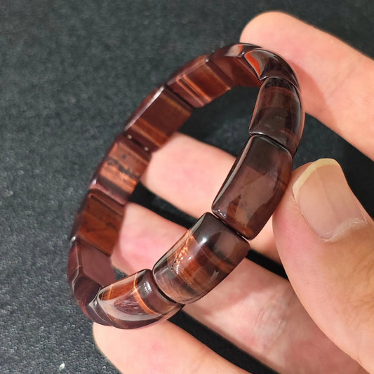 red tigers eye curved plate cuff bracelet held in hand showcasing deep mahogany red chatoyancy
