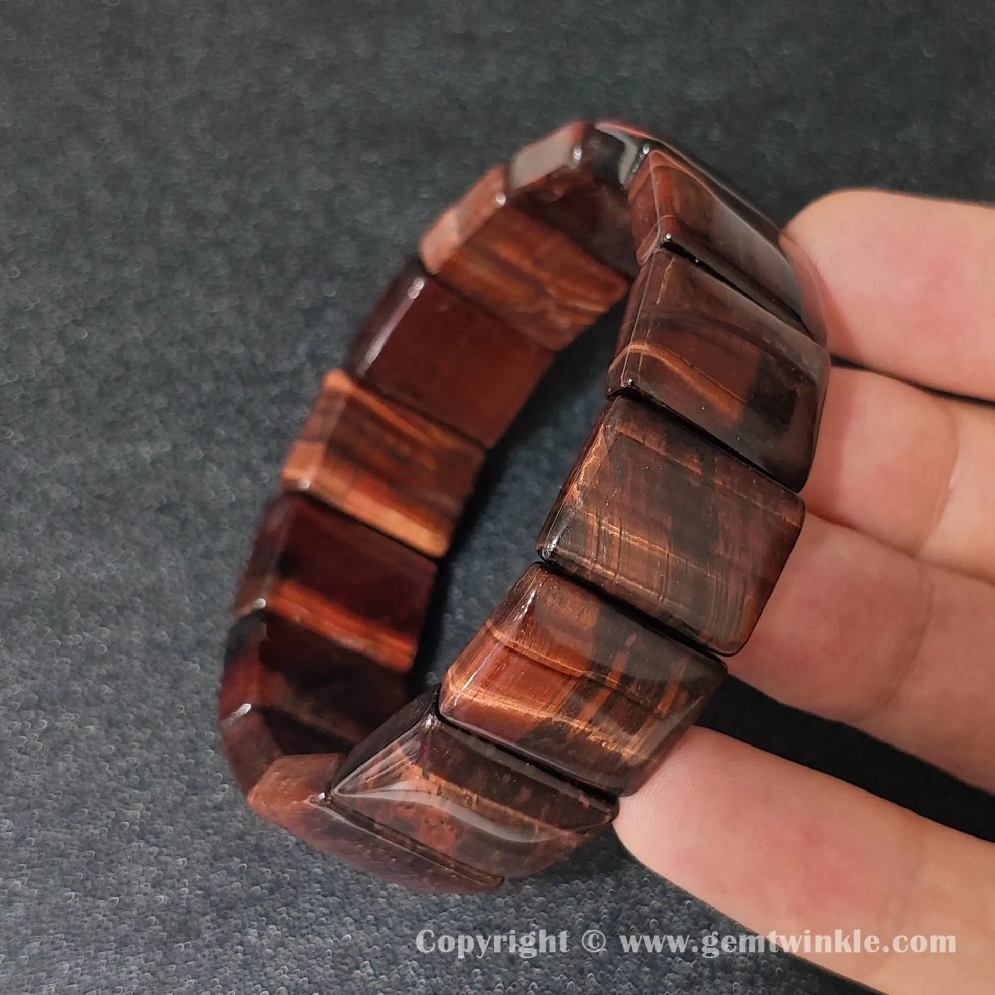 red tigers eye plate cuff bracelet featuring 20x15mm rectangular beads held in hand displaying rich mahogany sheen