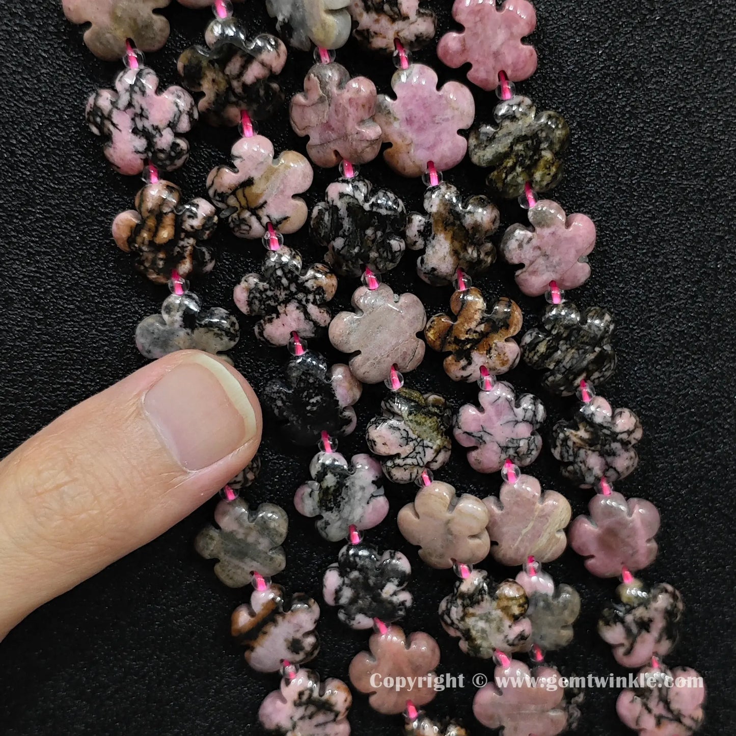 Close up view of rhodonite cherry blossom carved beads held on fingers for quality preview