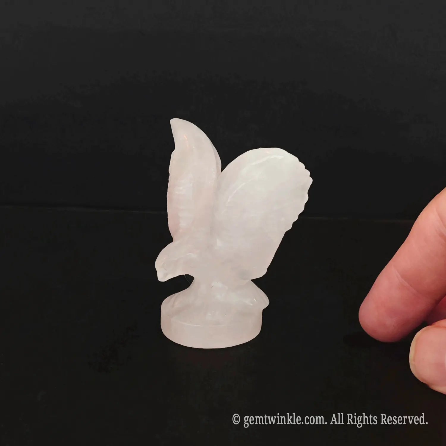 Side view of carved rose quartz crystal eagle showing detailed wing textures and sharp beak shape
