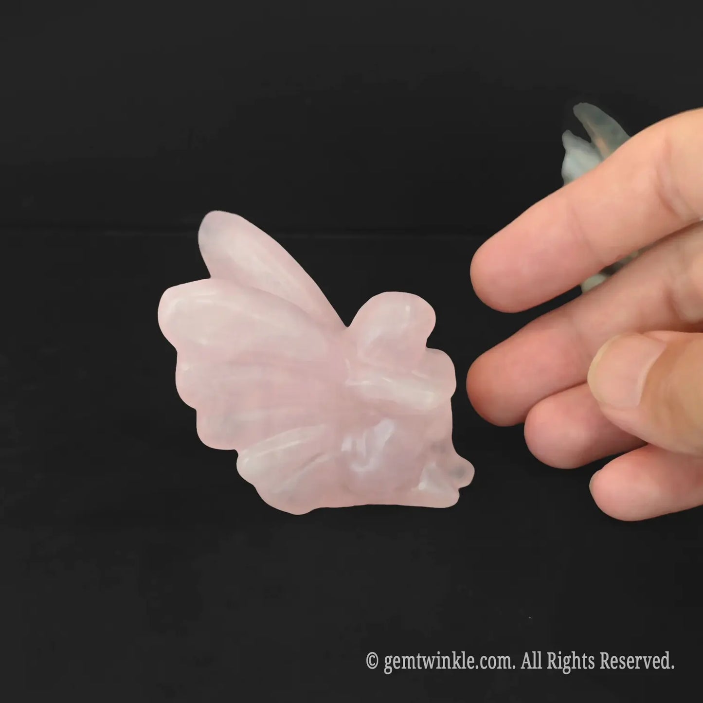 Carved pink rose quartz crystal flower fairy figurine resting on a flat polished base