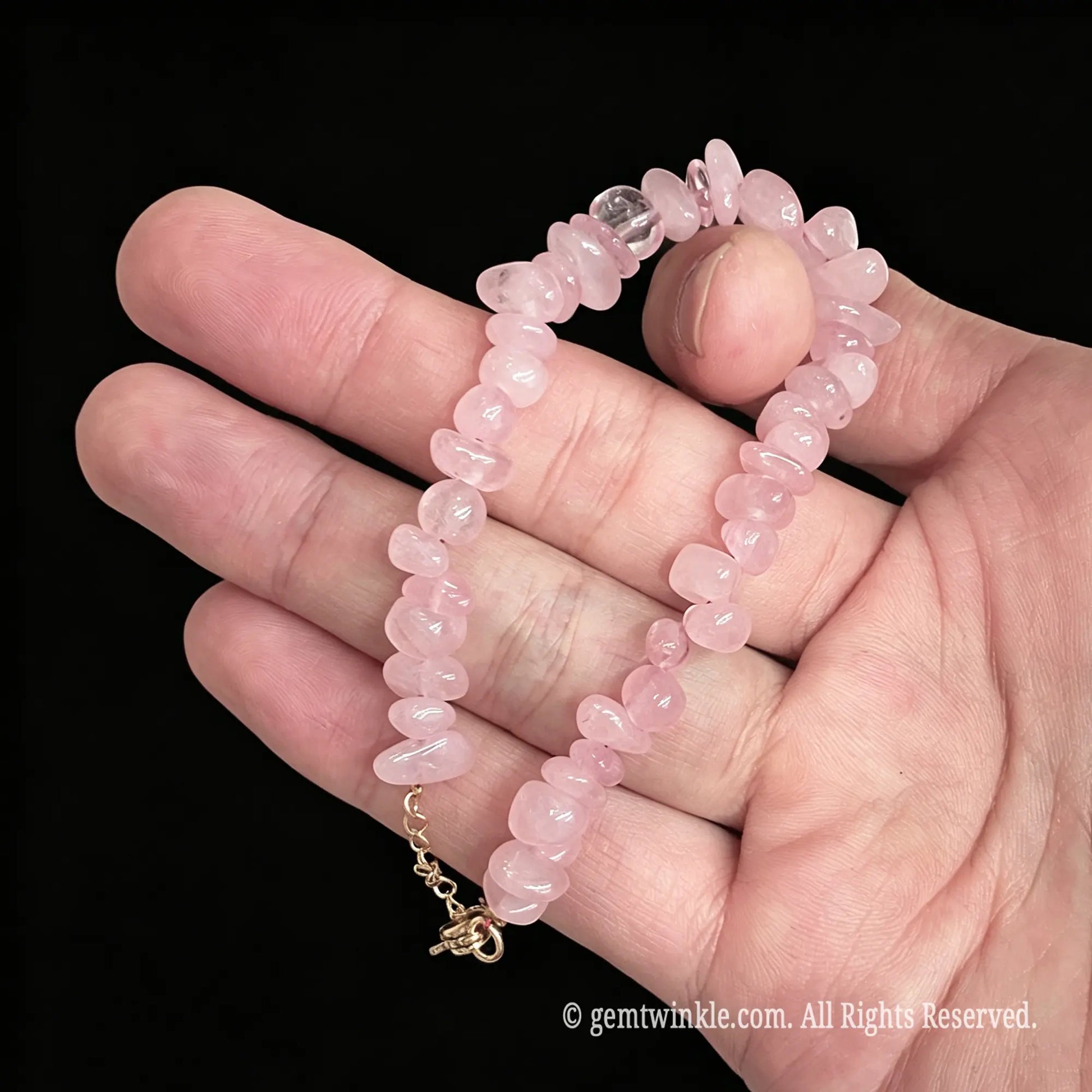 rose quartz gemstone bracelet held with finger showing gold tone extender chain